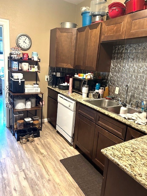 kitchen featuring light stone counters, a sink, light wood-type flooring, dishwasher, and baseboards