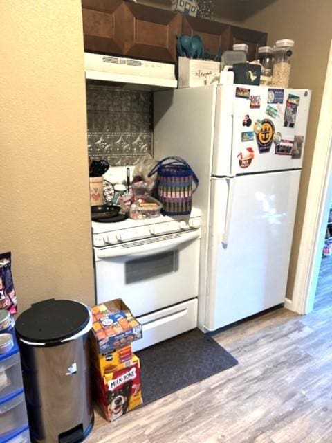 kitchen featuring white appliances, wood finished floors, and under cabinet range hood