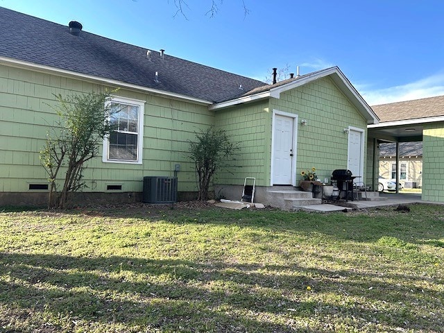 rear view of property featuring roof with shingles, a yard, central AC unit, crawl space, and a patio area