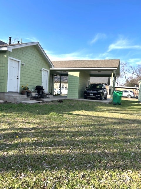 rear view of house featuring entry steps, an attached carport, a lawn, and a shingled roof