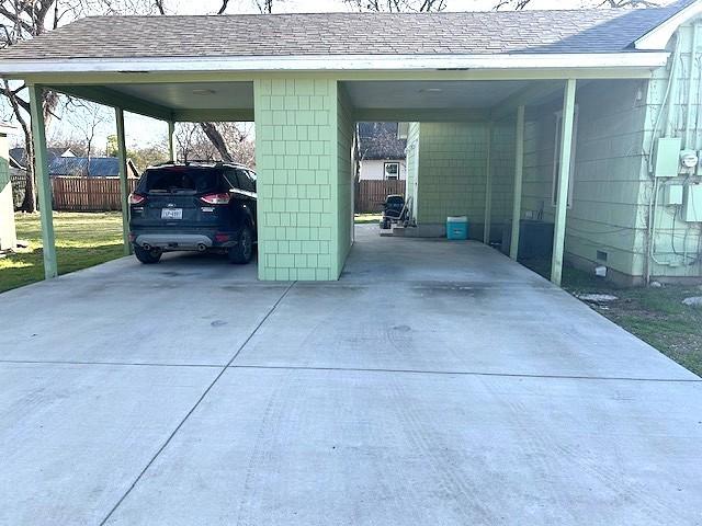 view of parking / parking lot with concrete driveway, a carport, and fence