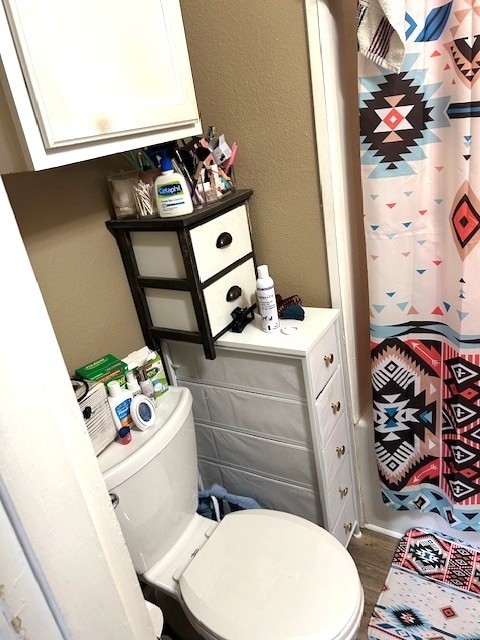 bathroom with curtained shower, a textured wall, toilet, and wood finished floors