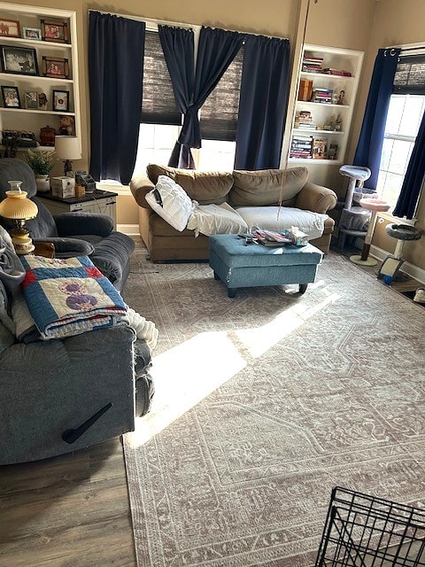 living room featuring built in shelves, baseboards, and wood finished floors