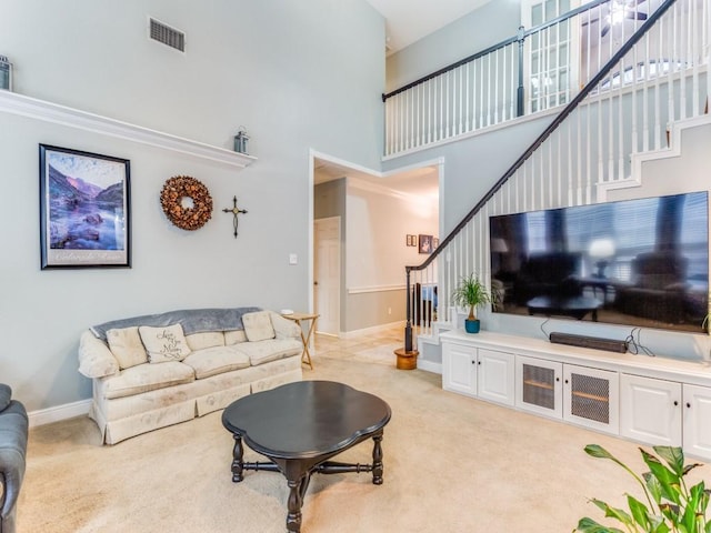 living room featuring light colored carpet, visible vents, a towering ceiling, and stairs