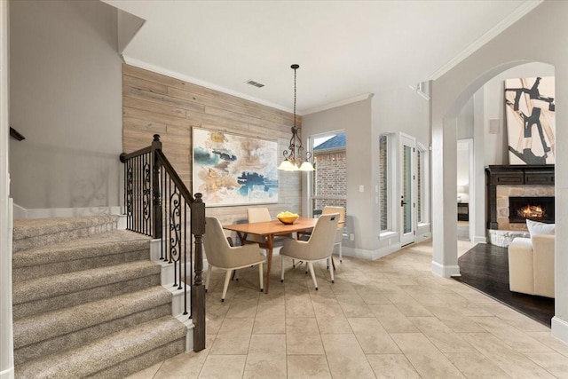 dining area featuring wood walls, a fireplace, visible vents, stairs, and crown molding