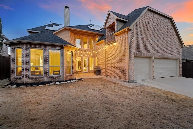 back of property with solar panels, brick siding, a chimney, and concrete driveway