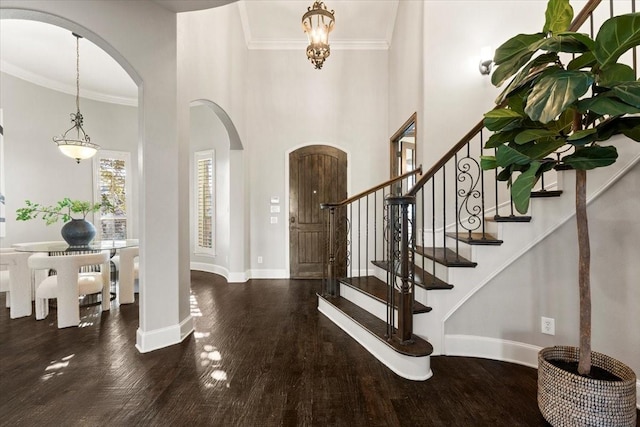 entryway featuring arched walkways, wood finished floors, baseboards, stairs, and ornamental molding