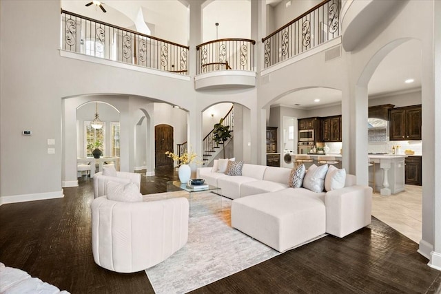 living area with arched walkways, visible vents, baseboards, stairway, and dark wood-style floors