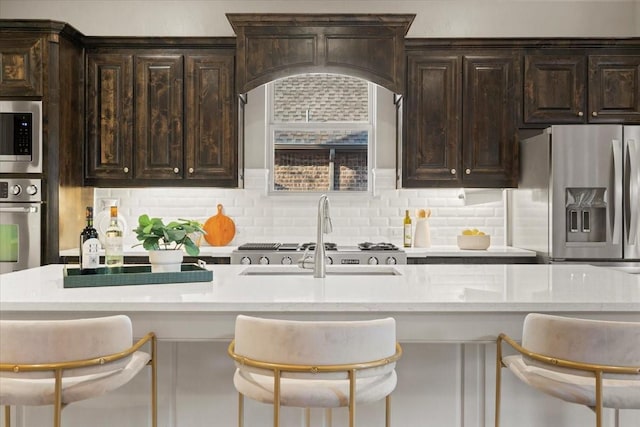 kitchen featuring light stone counters, dark brown cabinetry, stainless steel appliances, a sink, and tasteful backsplash