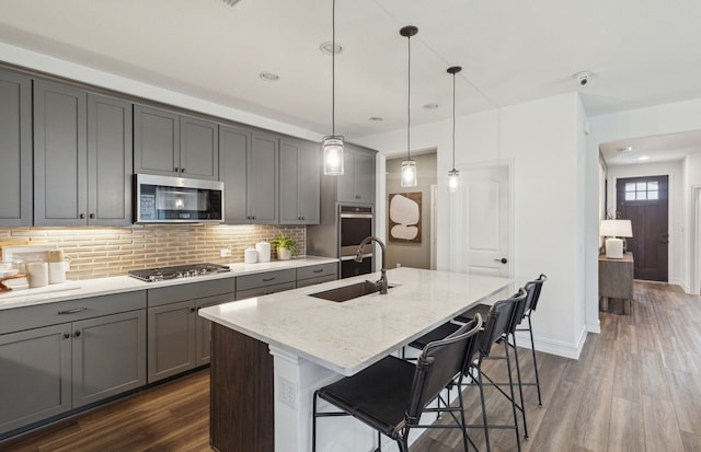 kitchen with a center island with sink, dark wood-style floors, gray cabinets, stainless steel appliances, and a sink