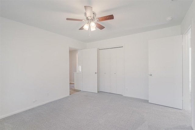 unfurnished bedroom with a closet, light colored carpet, ceiling fan, and baseboards