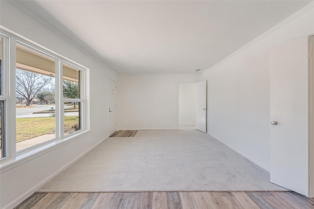 empty room with light wood-type flooring, light carpet, baseboards, and crown molding