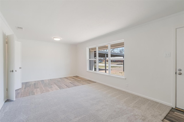 carpeted empty room featuring crown molding, wood finished floors, visible vents, and baseboards