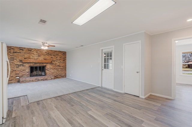 unfurnished living room with a ceiling fan, visible vents, a brick fireplace, light wood finished floors, and crown molding