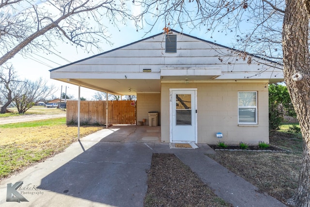 bungalow with a carport, concrete driveway, concrete block siding, and fence