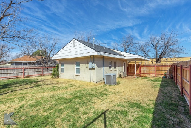 rear view of house with central AC unit, a fenced backyard, concrete block siding, and a lawn