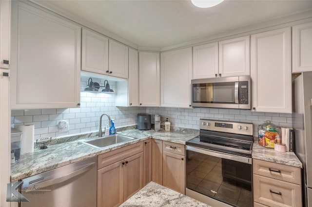 kitchen featuring light stone counters, appliances with stainless steel finishes, backsplash, and a sink