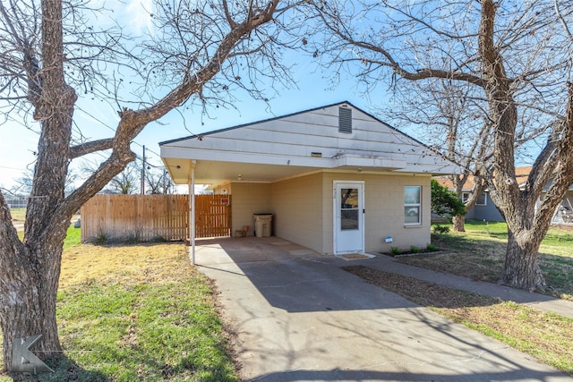 view of front of property featuring concrete block siding, fence, a carport, driveway, and a front lawn