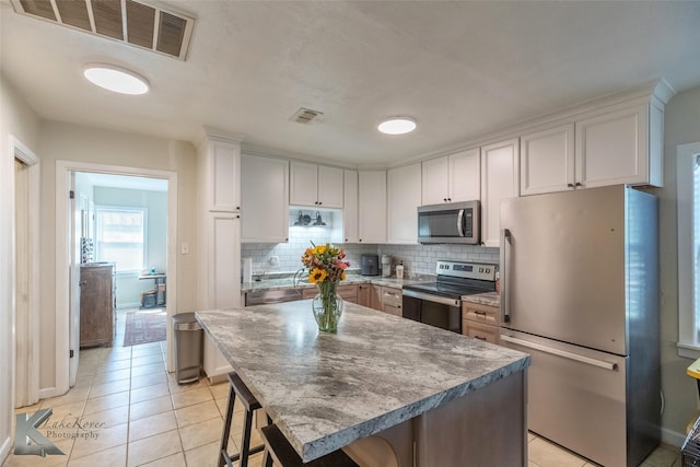 kitchen with stainless steel appliances, a breakfast bar, visible vents, and decorative backsplash