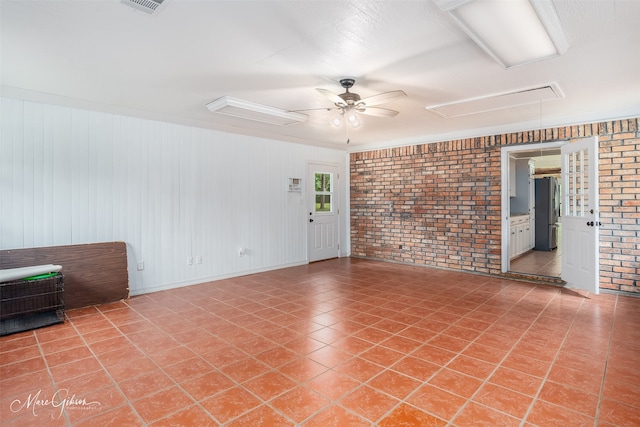 empty room with ceiling fan, light tile patterned floors, brick wall, visible vents, and attic access