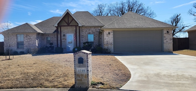 view of front of property featuring driveway, stone siding, roof with shingles, an attached garage, and brick siding