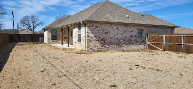 view of side of home with a fenced backyard, brick siding, and roof with shingles