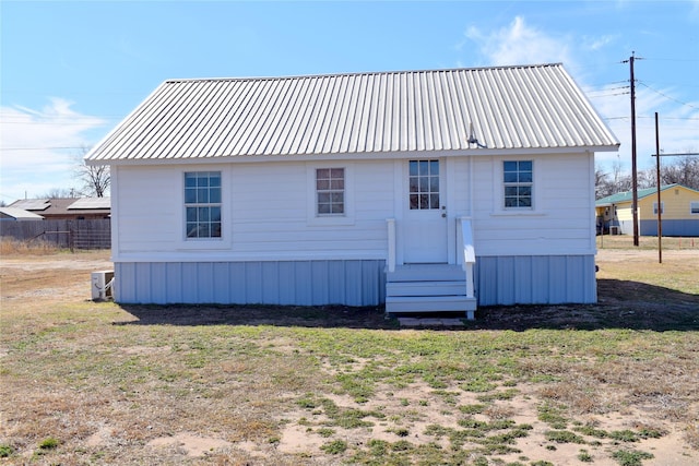 back of property featuring central air condition unit, metal roof, fence, and a lawn