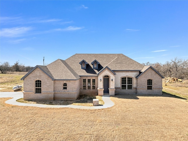 french country inspired facade with brick siding, a front lawn, and roof with shingles