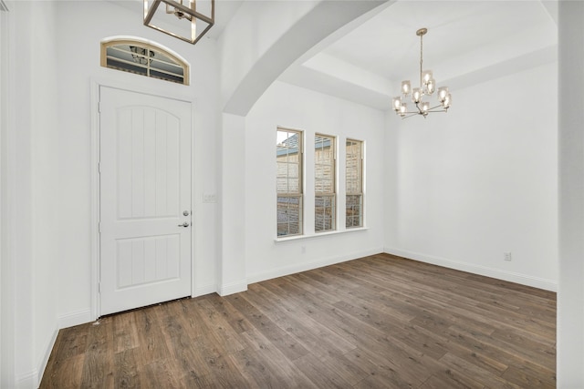 foyer with baseboards, dark wood-type flooring, arched walkways, and an inviting chandelier