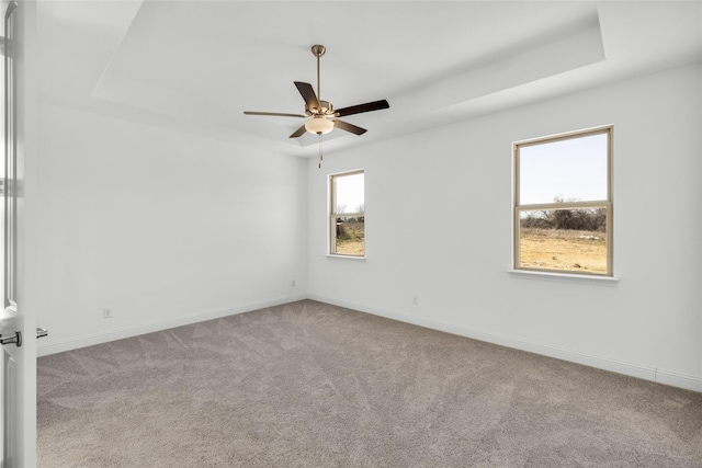 empty room with a ceiling fan, baseboards, a raised ceiling, and carpet flooring