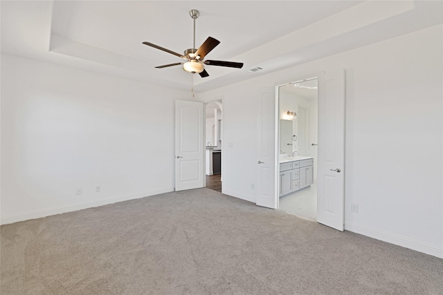 unfurnished bedroom featuring light carpet, a tray ceiling, arched walkways, and baseboards