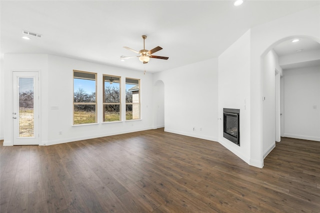 unfurnished living room featuring arched walkways, ceiling fan, a glass covered fireplace, and a wealth of natural light