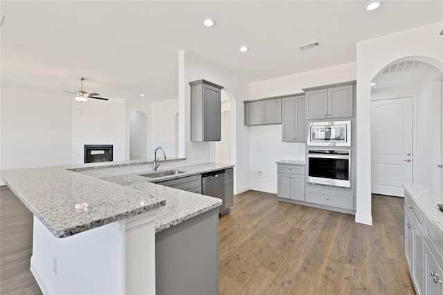 kitchen with light stone counters, arched walkways, visible vents, gray cabinetry, and appliances with stainless steel finishes