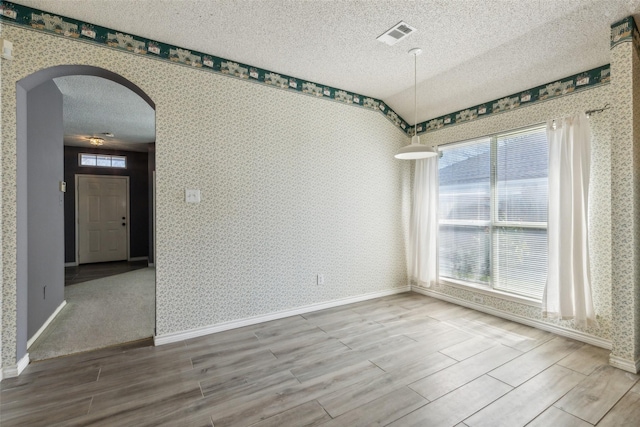 empty room featuring wallpapered walls, arched walkways, and a textured ceiling