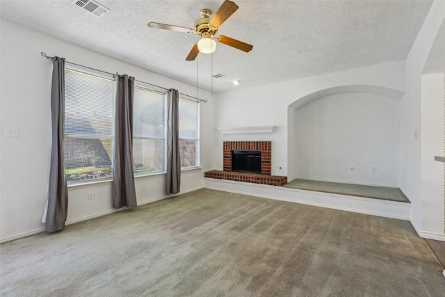 unfurnished living room featuring carpet, a fireplace, visible vents, a ceiling fan, and a textured ceiling