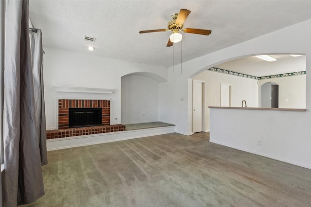 unfurnished living room with carpet, a fireplace, ceiling fan, and a textured ceiling