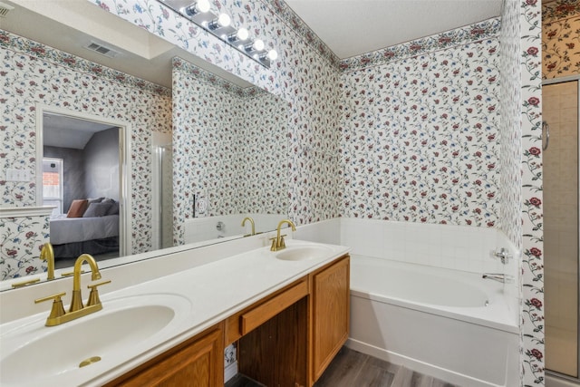 ensuite bathroom featuring a bath, a sink, ensuite bathroom, and wallpapered walls