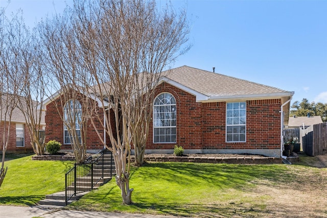 view of front of house with a shingled roof, fence, a front lawn, and brick siding