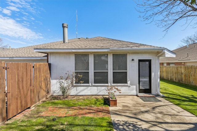 back of property with a patio area, roof with shingles, fence, and a lawn