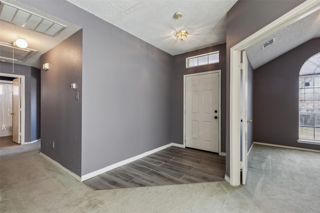 foyer with visible vents, vaulted ceiling, a textured ceiling, and baseboards