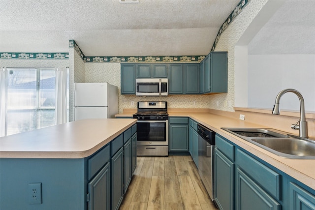 kitchen with wallpapered walls, appliances with stainless steel finishes, a textured ceiling, light wood-type flooring, and a sink