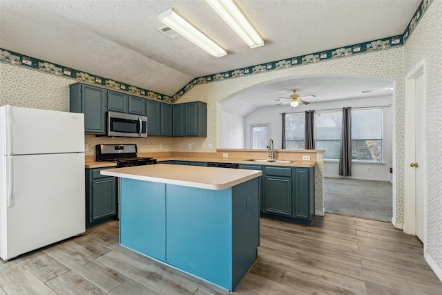 kitchen featuring arched walkways, stainless steel microwave, freestanding refrigerator, a sink, and wallpapered walls