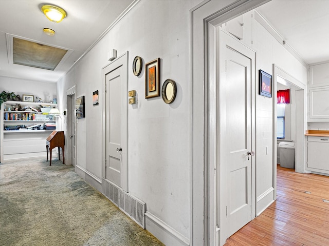 hall featuring light wood finished floors, ornamental molding, light carpet, and visible vents