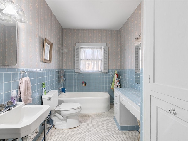 bathroom with a wainscoted wall, wallpapered walls, toilet, a sink, and a bath