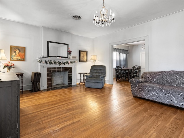 living room with baseboards, visible vents, a tiled fireplace, wood finished floors, and a chandelier