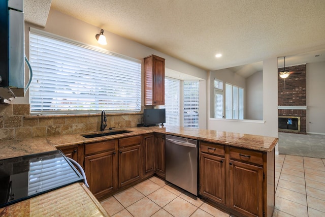 kitchen with light tile patterned floors, a peninsula, a sink, stainless steel dishwasher, and a brick fireplace