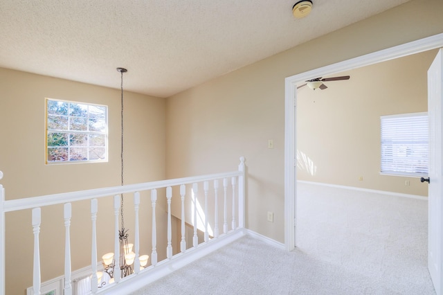 hallway featuring carpet, baseboards, a textured ceiling, and an upstairs landing