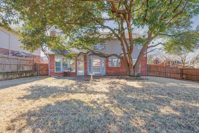 back of house featuring a fenced backyard, a lawn, and brick siding