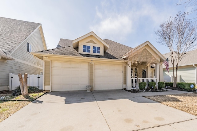 view of front of house featuring a garage, a shingled roof, concrete driveway, fence, and a porch