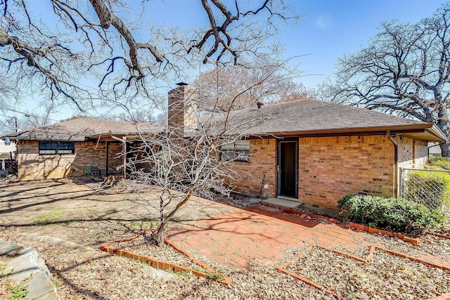 back of property with a patio, brick siding, a chimney, and roof with shingles